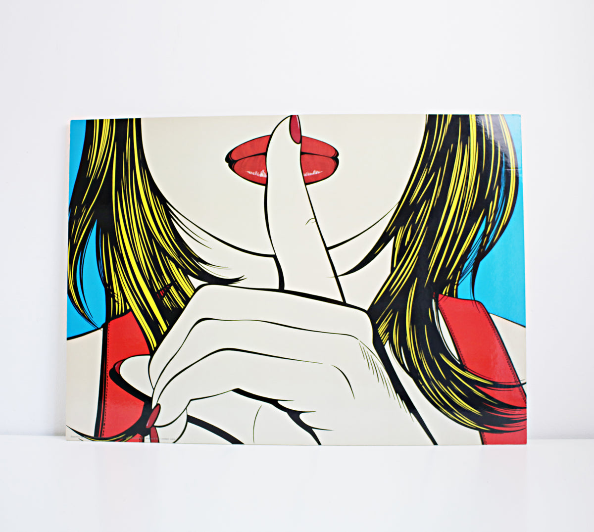 A pop art style print or poster showing a close-up illustration of a woman with yellow hair, red lips, and a hand covering part of her face, displayed against a plain white wall. IKEA Solmyra print 1999